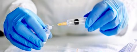 A pharmacist pulls a vaccine into a syringe from a vial. 