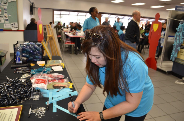 Denim Day supporter is shown writing the name of a sexual assault victim on a blue ribbon. The blue ribbon symbolizes sexual assault victims. While the teal ribbon symbolizes child abuse victims.