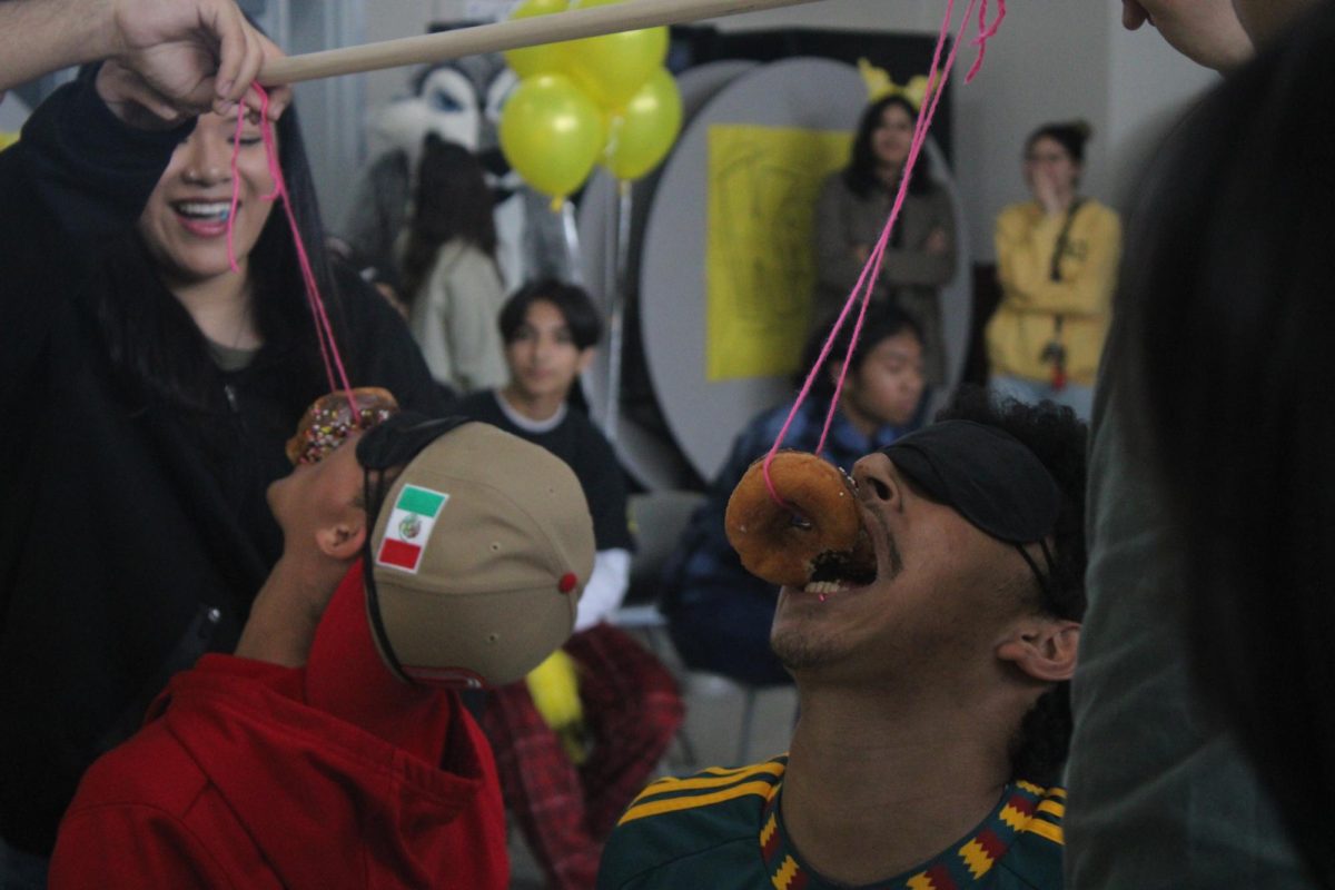 ASB member Nadia Tay holds up a stick with donuts on string for a House Competition game, as teammates Christian Aleman (9) and Adrian Cordon (12)